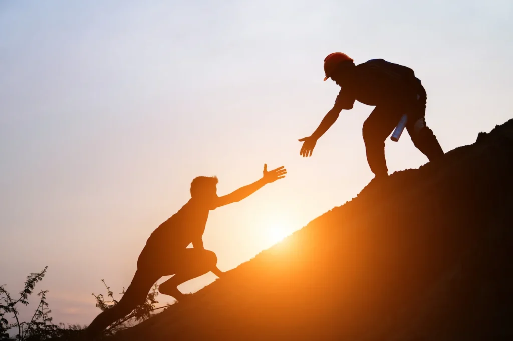 Mann hilft anderem den Berg hinauf – Symbol für transgenerationales Coaching